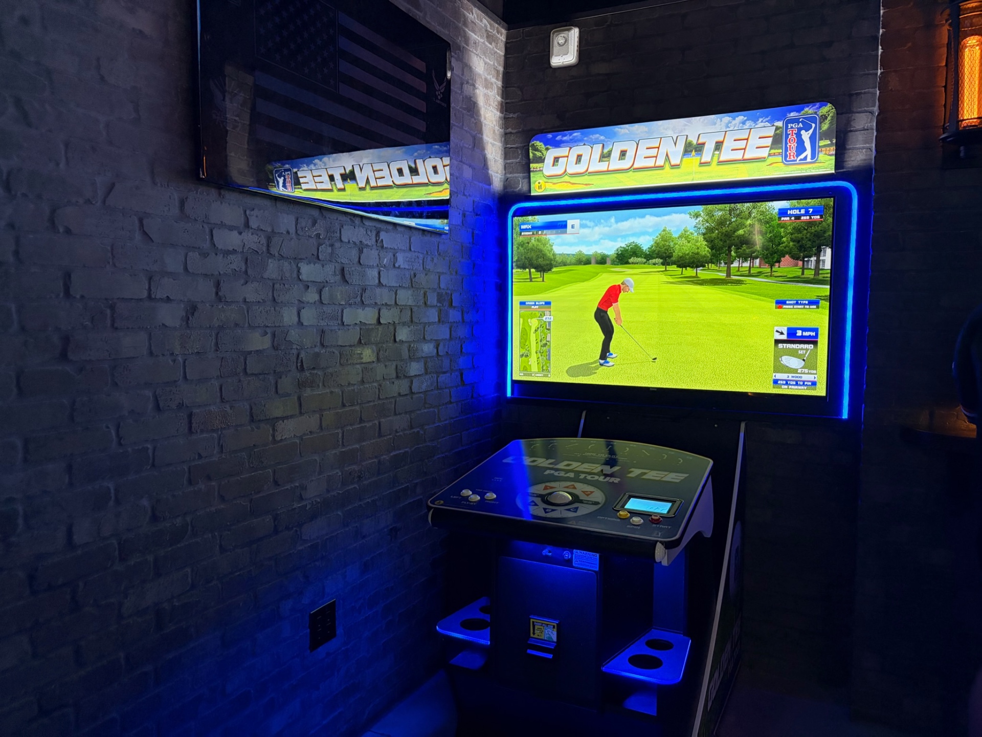 Golden Tee PGA Tour arcade cabinet glowing blue in a brick nook