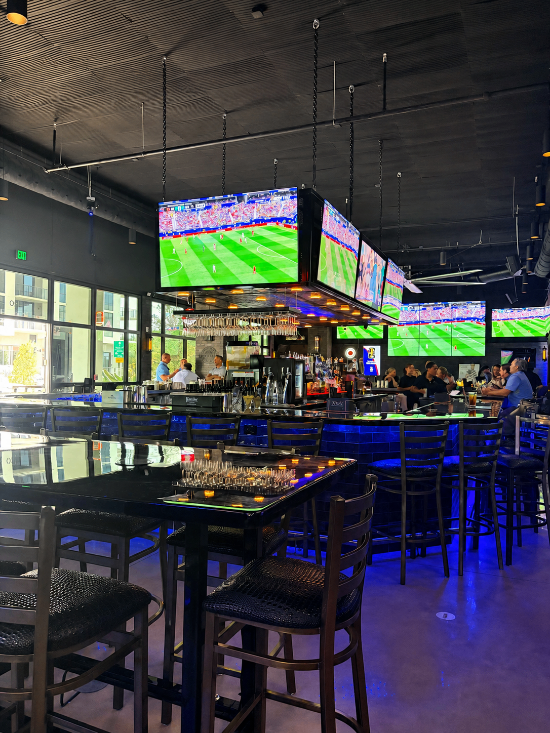 Main bar with hanging TVs showing soccer and blue-lit bar seating