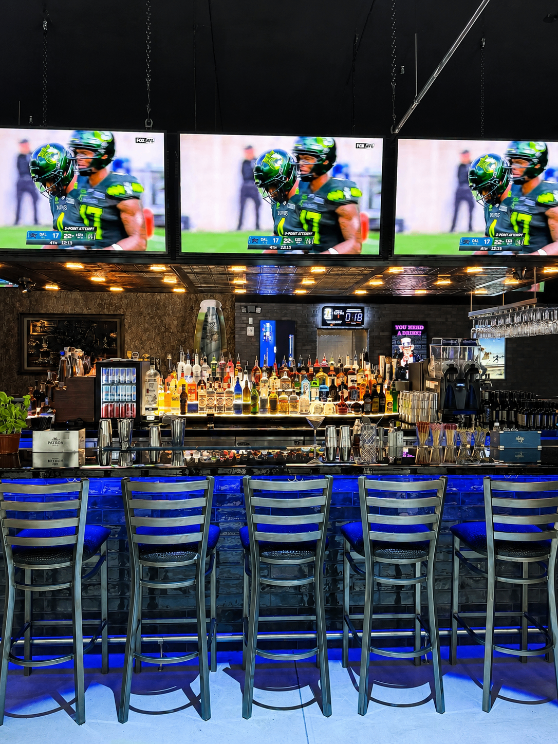 Bar stools facing TVs showing an NFL game above the liquor shelves